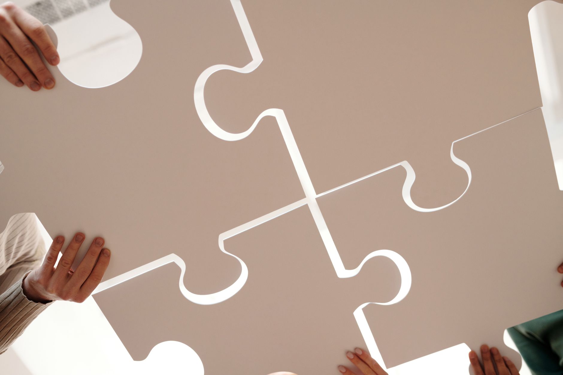 Two hands holding large interlocking puzzle pieces in a bright space.